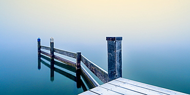 Snow-covered jetty in marina at misty sunrise on Lake Starnberg, Seeshaupt, Bavaria, Germany