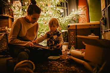 little boy with his mother looking at book in front of the Christmas tree, Christmas, family