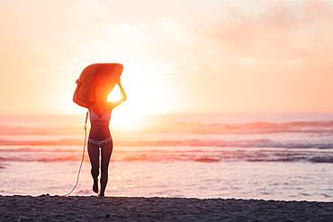 Female surfer goes with surfboard on the beach in sunset, surfing, Portugal, sunset