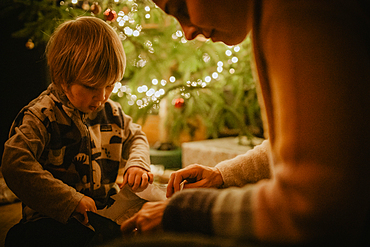 little boy unwraps his gifts in front of the Christmas tree, Christmas, family