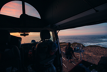 Woman sitting in front of her camper while having breakfast with the coast of Portugal in view, vacation, camping, Portugal