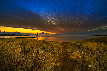 Herd Groyne Lighthouse and dramatic sunset with glowing clouds and beach grass in the foreground, South Shields, Tyne and Wear, England