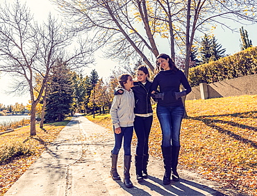 A mother and her two daughters walking and talking on a pathway in a city park on a warm autumn day, Edmonton, Alberta, Canada