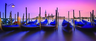 Gondolas moored along the shoreline of the Grand Canal during a vibrant sunset with a view of San Giorgio Maggiore and church in the distance, Venice, Italy