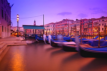 Gondolas moored along the shoreline of the Grand Canal during a vibrant sunset, Venice, Italy