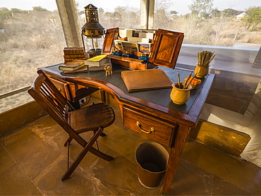 Desk in the foyer of a tent surrounded by windows with a view out to a landscape of dry brush and trees, Rajasthan, India