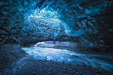 Man standing under an opening in the ice cave while walking beneath a glacier: Iceland