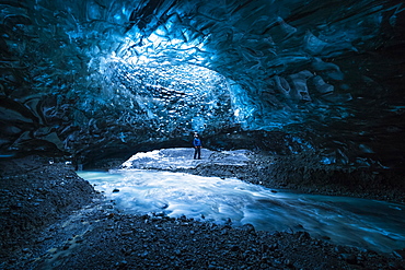 Man standing under an opening in the ice cave while walking beneath a glacier: Iceland