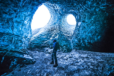 Person standing underneath the openings of a glacier, South Iceland, Iceland