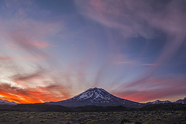 The snow-covered slopes of a volcano are set against a red sunset sky, Mendoza, Argentina