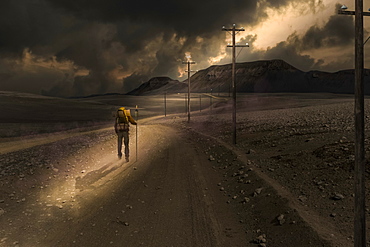 A man walks along an empty road in a sunbeam shining through dark clouds, composite image