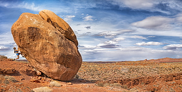 A woman hangs on the side of boulder in the Valley of the Gods, Utah, United States of America