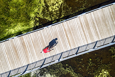 Aerial view looking straight down on a female cyclist on a bridge across a swampy pond with shadow of cyclist, East of Calgary, Alberta, Canada