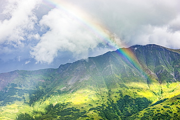 A rainbow shines through atmospheric light, lush green mountainsides in the background, Hatcher Pass, South-central Alaska, Palmer, Alaska, United States of America