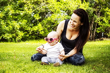 Portrait of a young mother spending quality time with her daughter in a park during the summer and the baby is wearing funny sunglasses, Edmonton, Alberta, Canada