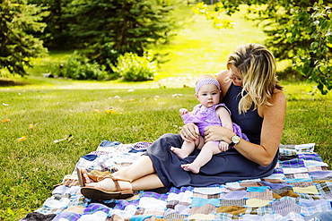 A mother and her baby daughter sitting on a picnic blanket and spending quality time together while enjoying a family outing in a city park on a warm fall afternoon, Edmonton, Alberta, Canada