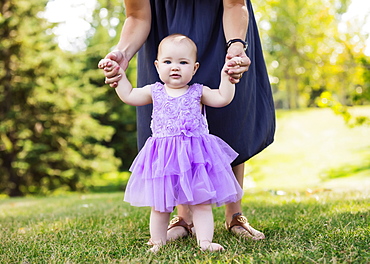 A mother teaching her baby daughter how to walk in a city park on a warm fall afternoon: Edmonton, Alberta, Canada