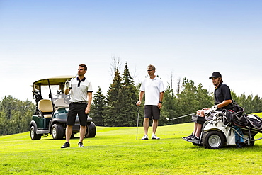 A group of golfers, one of which is handicapped with a mobility assistance device, watching as a long drive as it makes its way down a fairway, Edmonton, Alberta, Canada