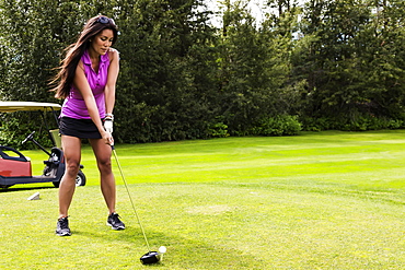 A female golfer lines up her driver to the golf ball as she sets up her shot on a tee, Edmonton, Alberta, Canada