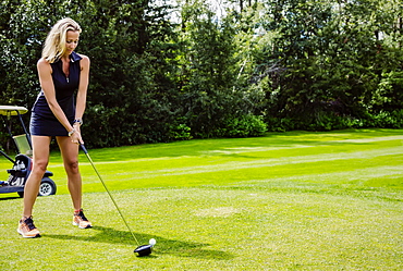 A female golfer lines up her driver to the golf ball as she sets up her shot on a tee, Edmonton, Alberta, Canada