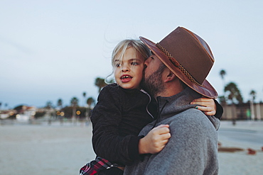 A father and daughter having a tender moment, the father holding his daughter in an embrace on a beach at dusk, Long Beach, California, United States of America