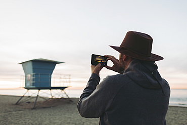 A man stands photographing a lifeguard station at dusk, Long Beach, California, United States of America