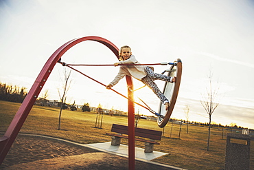 A daring young girl playing on saucer swings in a playground on a warm autumn evening, Edmonton, Alberta, Canada