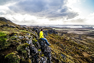 Man looks out over the ocean while sitting on a cliff, Iceland