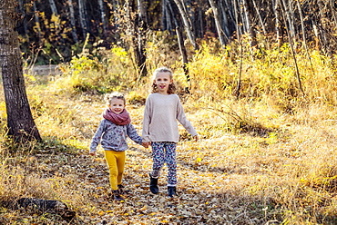 Two young girls who are sisters running through the woods in a city park on a warm fall evening, Edmonton, Alberta, Canada