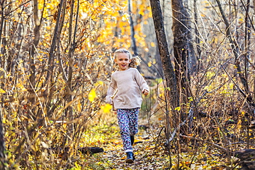 A young girl running through the woods in a city park on a warm fall evening, Edmonton, Alberta, Canada