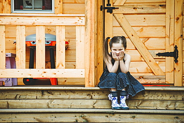 Portrait of a young girl sitting on a step in front of a wooden door, Alberta, Canada