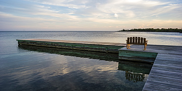 A wooden bench on a dock facing the coastline and open ocean at sunrise, Belize