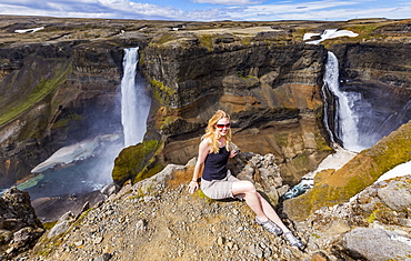 A young female hiker poses for a portrait on the edge of a stunning waterfall valley known as Haifoss, in Southern Iceland, Iceland