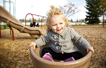 A cute young girl spinning in a saucer on a playground during the fall season, Spruce Grove, Alberta, Canada