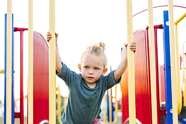 A young girl with blond hair playing in a playground and climbing up a rock ladder on a warm fall day, Spruce Grove, Alberta, Canada