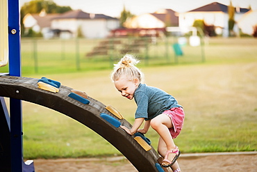 A young girl with blond hair playing in a playground and climbing up a rock ladder on a warm fall day, Spruce Grove, Alberta, Canada