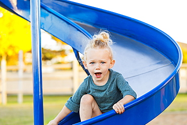 A young girl with blond hair playing in a playground and going down a slide on a warm fall day, Spruce Grove, Alberta, Canada