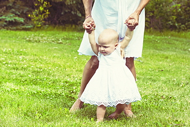 A young mom teaching her baby daughter to walk in a park on a beautiful warm sunny day, Edmonton, Alberta, Canada