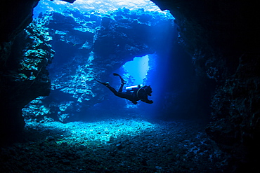 Scuba diver swims through lava arches with sun rays, Cathedrals dive site, Lanai City, Lanai, Hawaii, United States of America