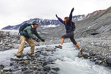 A wife jumps to her husband across an icy stream while hiking near Gulkana Glacier, Alaska, United States of America