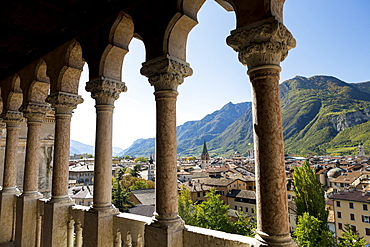 Palace stone columns frames an alpine village in the background with mountains and blue sky, Trento, Trento, Italy