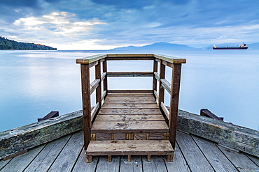 A wooden viewing platform at the end of a dock looks out to a ship on the tranquil ocean, Vancouver, British Columbia, Canada