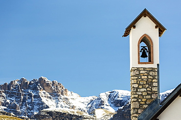 Stone church bell tower with snow-covered mountain range in the background with blue sky, Sesto, Bolzano, Italy