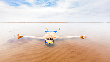 A man wearing a bathing suit floats in the shallow ocean water with his body outstretched and looking up to the sky, Prince Edward Island, Canada