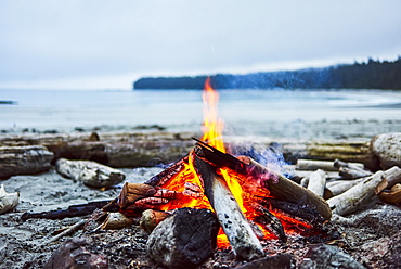 A fire on the beach with the ocean and coastline in the background, Cape Scott Provincial Park, British Columbia, Canada