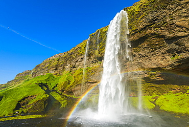 Skogafoss waterfall with blue sky and a rainbow in the mist, Iceland