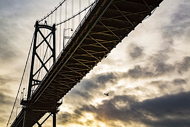 Low angle view of a bridge at sunset with an airplane flying in the distance, Vancouver, British Columbia, Canada