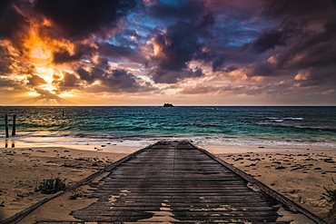 A wooden boardwalk on a beach leading to the turquoise water of Hamelin Bay at sunset, Western Australia, Australia