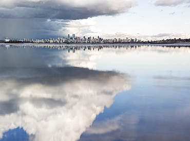 Distant view of the Vancouver skyline over the Pacific Ocean reflecting clouds, viewed from Spanish Banks, Vancouver, British Columbia, Canada