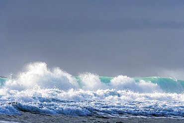 Sunlight shines on a wave under a cloudy sky along the Oregon coast, Lincoln City, Oregon, United States of America